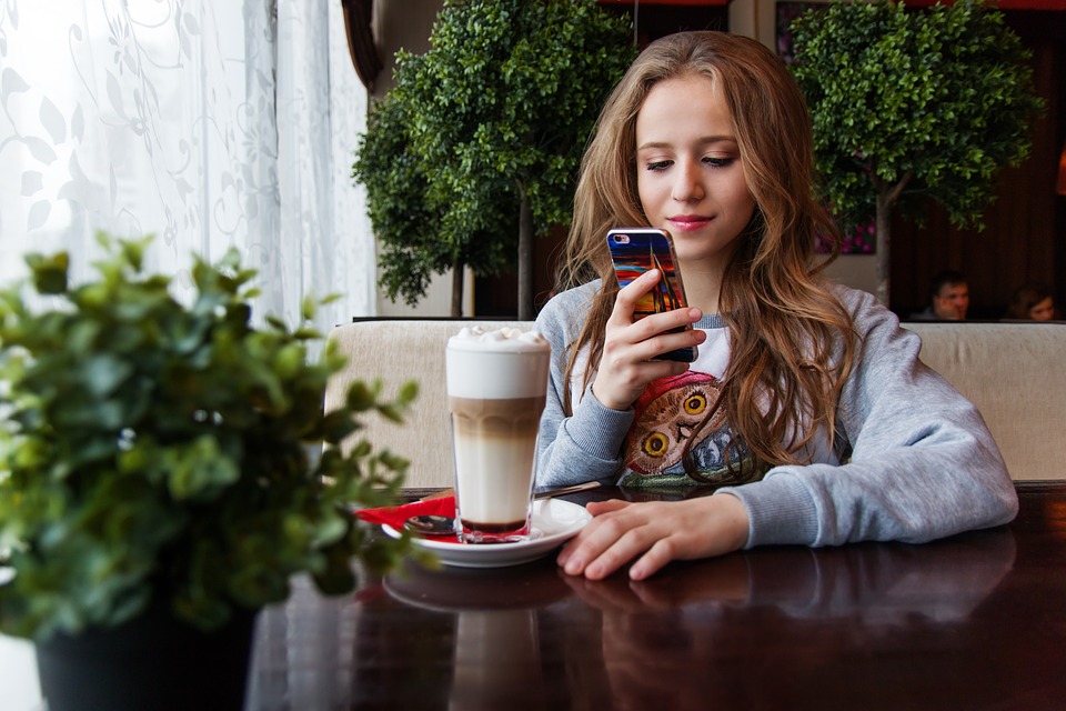 Mädchen im Cafe mit Smartphone und Milchkaffee